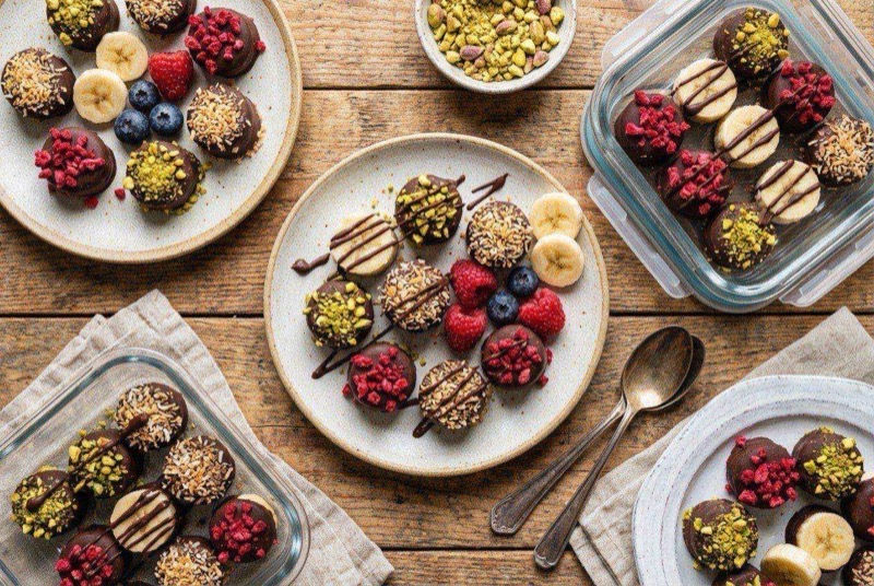 Frozen banana slices dipped in dark chocolate with crushed peanut toppings on parchment paper