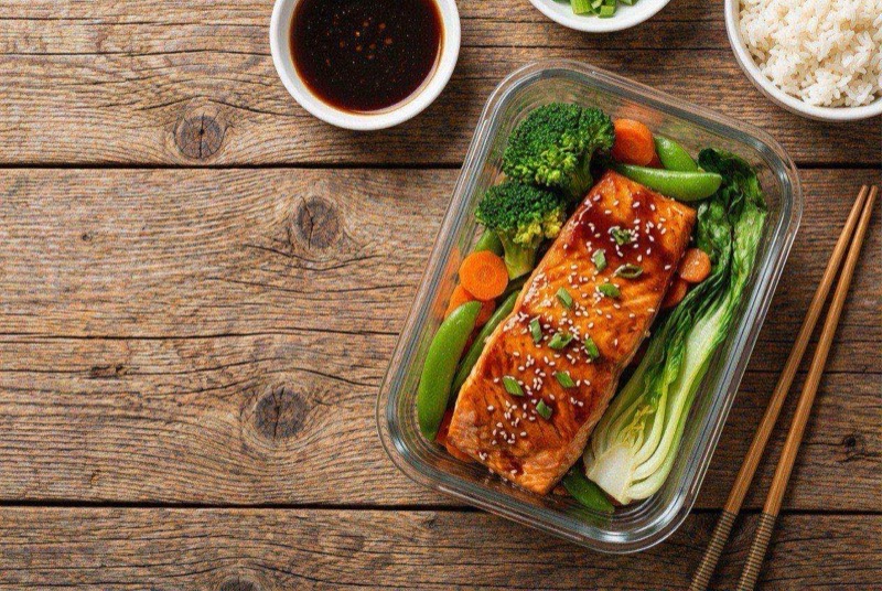 Teriyaki-glazed salmon fillet on a plate with sesame-dressed broccoli and snap peas
