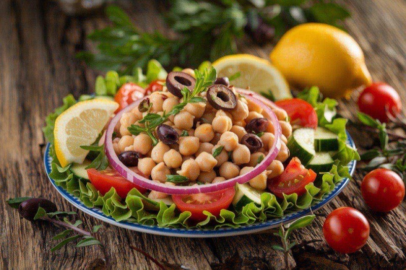 Colorful Mediterranean chickpea salad in a clear meal-prep container with visible olives, tomatoes, and cucumber