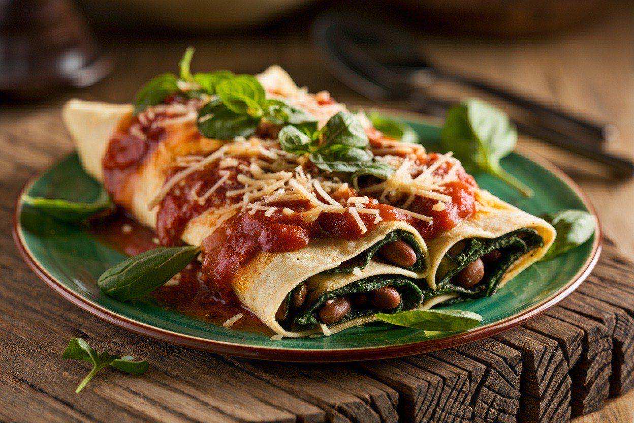 Sliced enchilada casserole in a baking dish showing layers of corn tortillas, spinach, beans, and red sauce