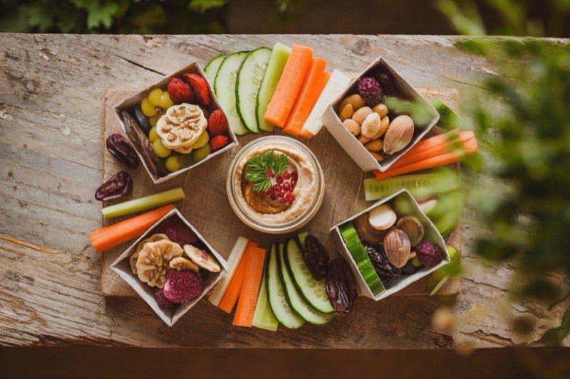 Snack boxes with small container of hummus surrounded by colorful cut vegetables in neat compartments