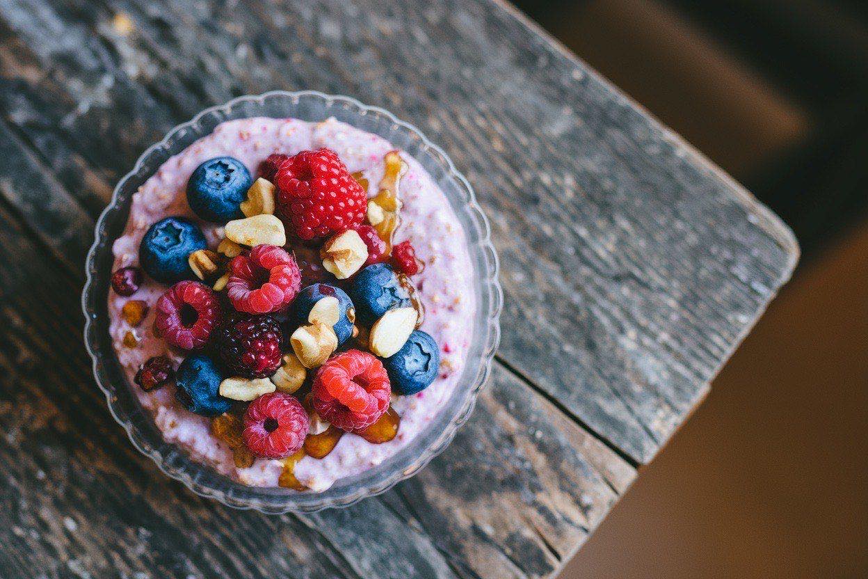 Five mason jars of overnight oats topped with fresh blueberries, strawberries, and raspberries lined up on a counter